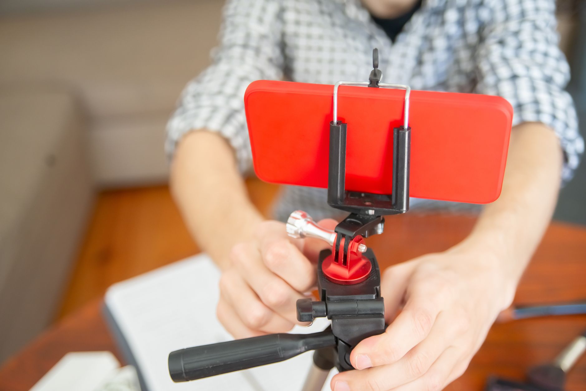 Primo piano di due mani che fissano uno smartphone con custodia rossa a un cavalletto, in un ambiente domestico.